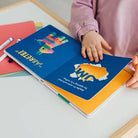 Child holding a colorful book with a blue cover featuring a cartoon character.