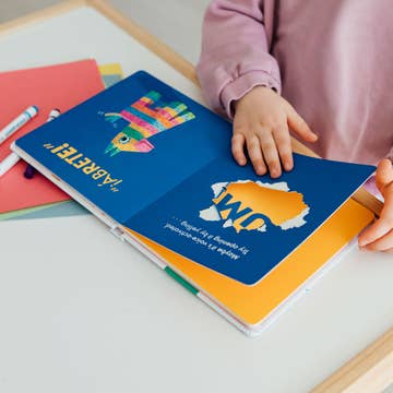 Child holding a colorful book with a blue cover featuring a cartoon character.