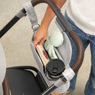 Person using a stroller organizer with a cup, books, and a blanket.