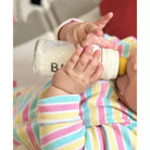 Baby's hands holding a bottle with colorful sleeves