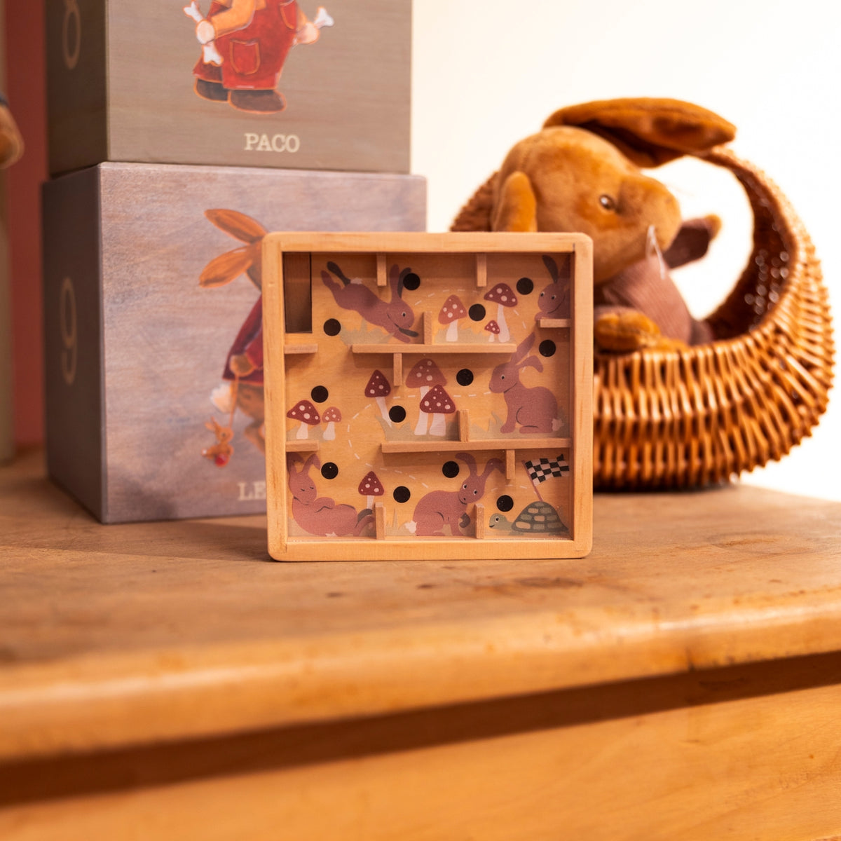 Wooden puzzle toy with animal and mushroom design on a wooden surface, with packaging and plush toy in the background.