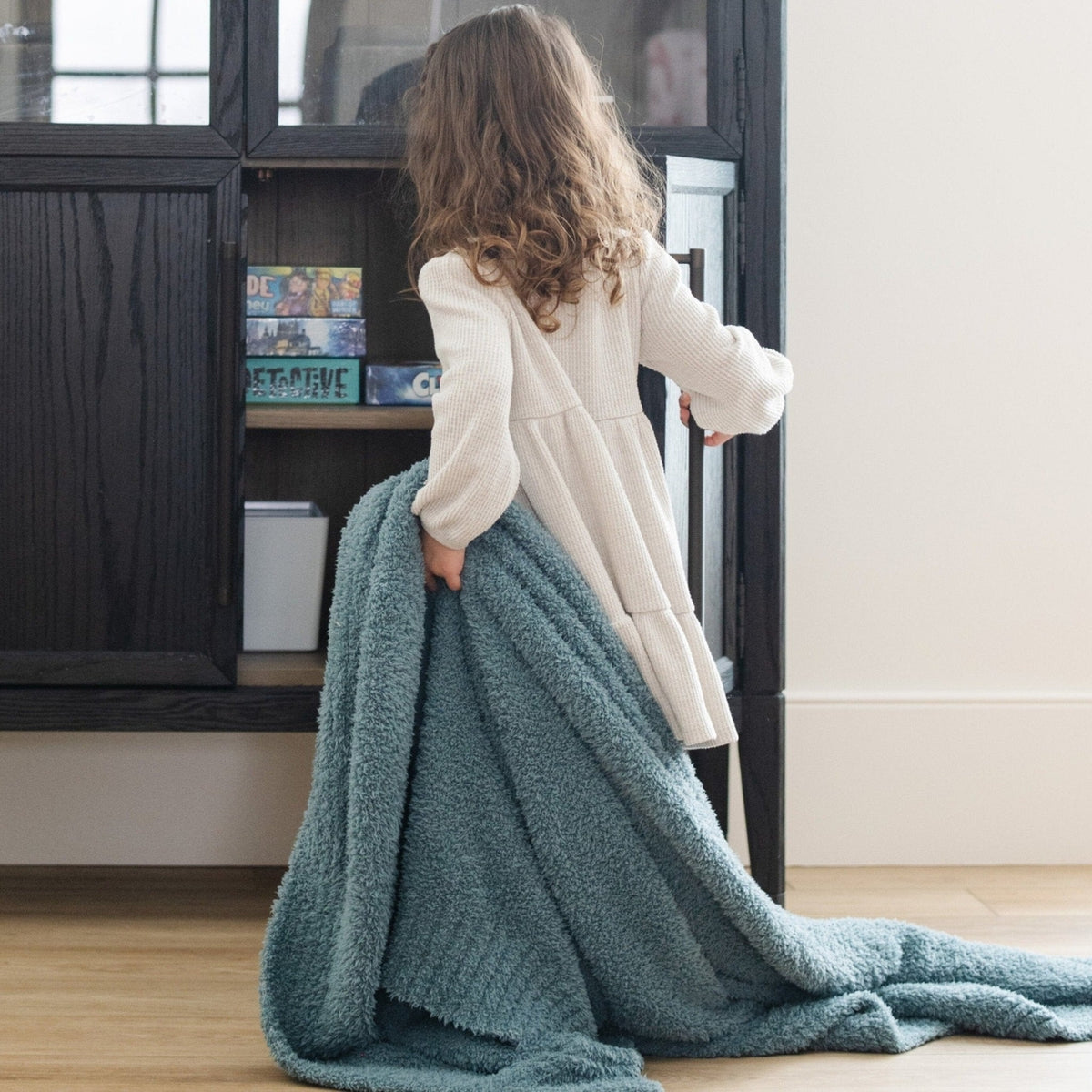 Person holding a large teal blanket in front of a bookshelf.