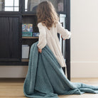 Person holding a large teal blanket in front of a bookshelf.