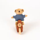 A small plush teddy bear wearing a blue knit sweater and riding a brown toy scooter, photographed against a clean white background.