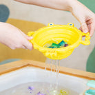 Yellow bath toy with water flowing out, held over a bathtub.