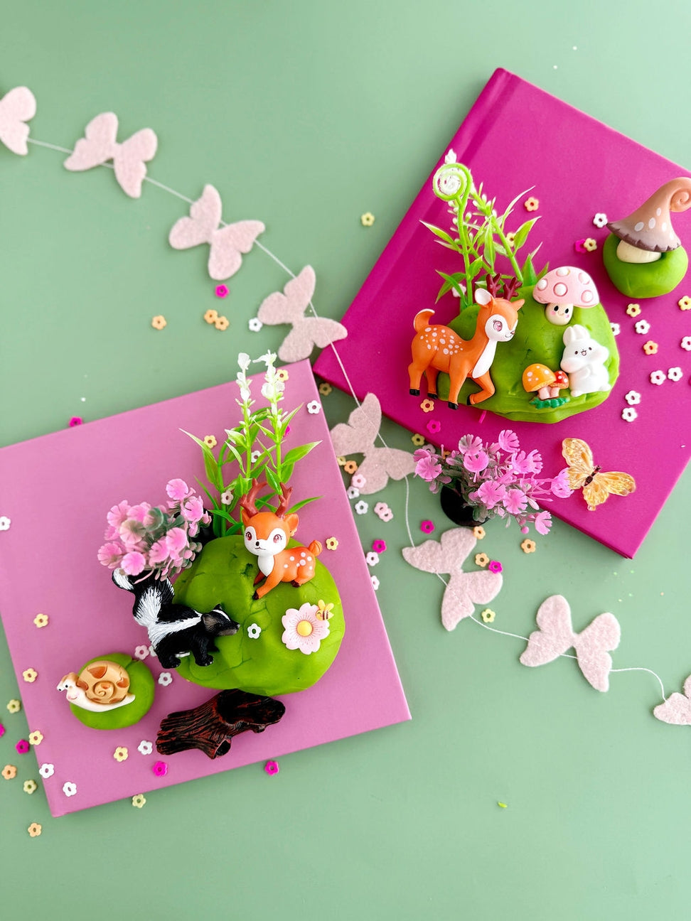 Two pink books with green landscapes featuring animals and flowers on a light green background.
