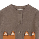 A close-up of a brown knit cardigan featuring two front pockets with fox-ear appliques in orange-brown and white, and brown buttons down the front.