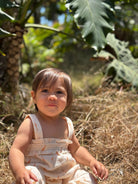 Child sitting on dry grass with green foliage in the background