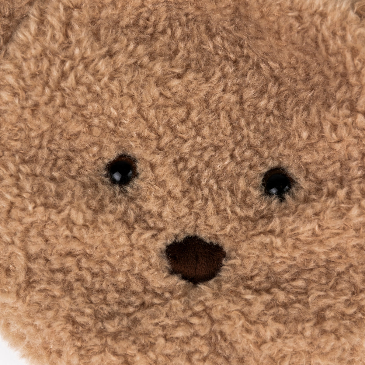 Close-up of a brown plush teddy bear face with black embroidered eyes and nose on a white background.