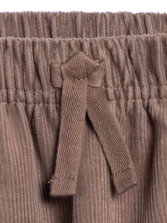 Close-up of a ribbed knit garment in a warm taupe-brown color, showing a gathered waistband and a matching fabric tie detail.