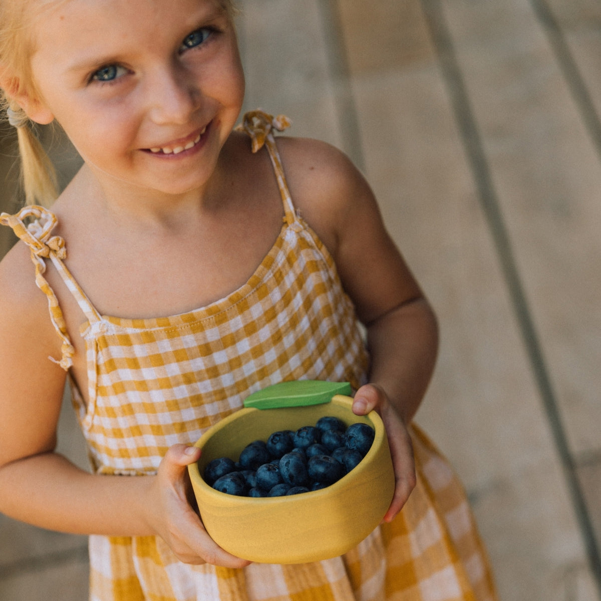 Young girl holding a bowl of blueberries on a stone surface