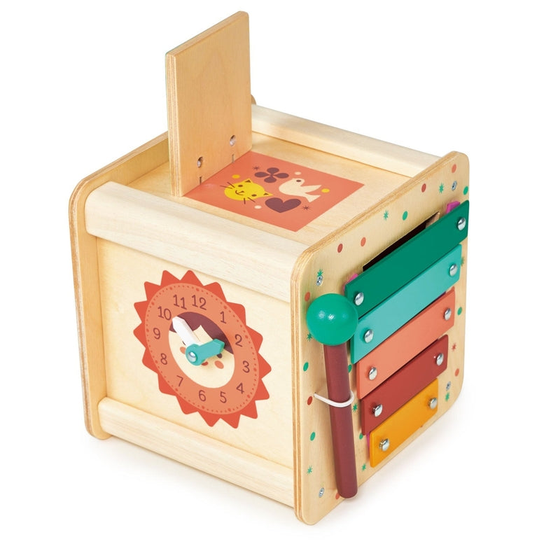 A wooden activity cube by Mentari on a plain white background, featuring a colorful clock face on the front, interlocking gears on the side, and an illustrated sliding puzzle top.
