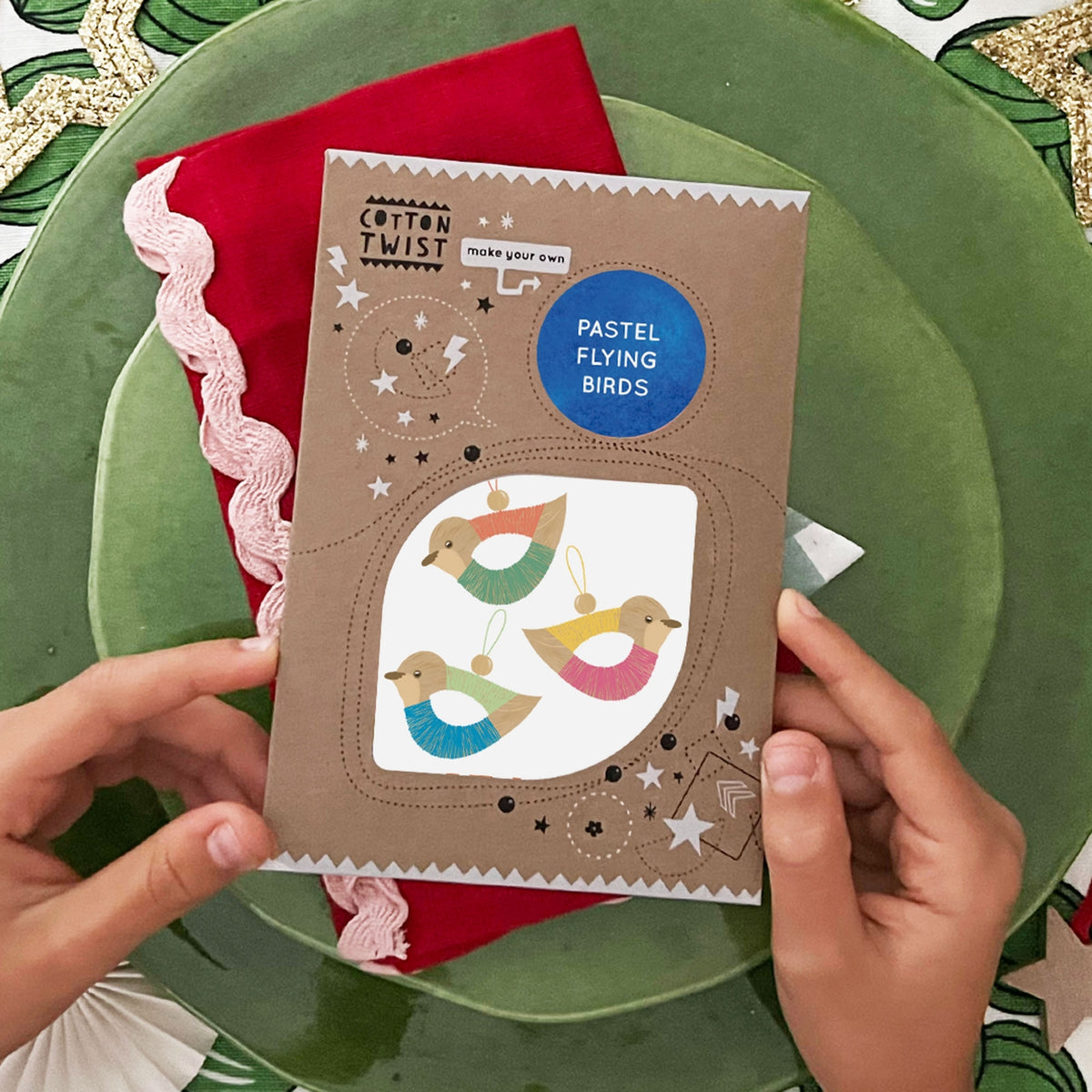 Cardboard craft kit with bird designs held by hands on a green plate.