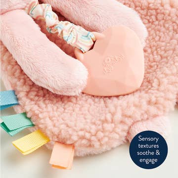 Pink plush toy with colorful tags on a soft pink background