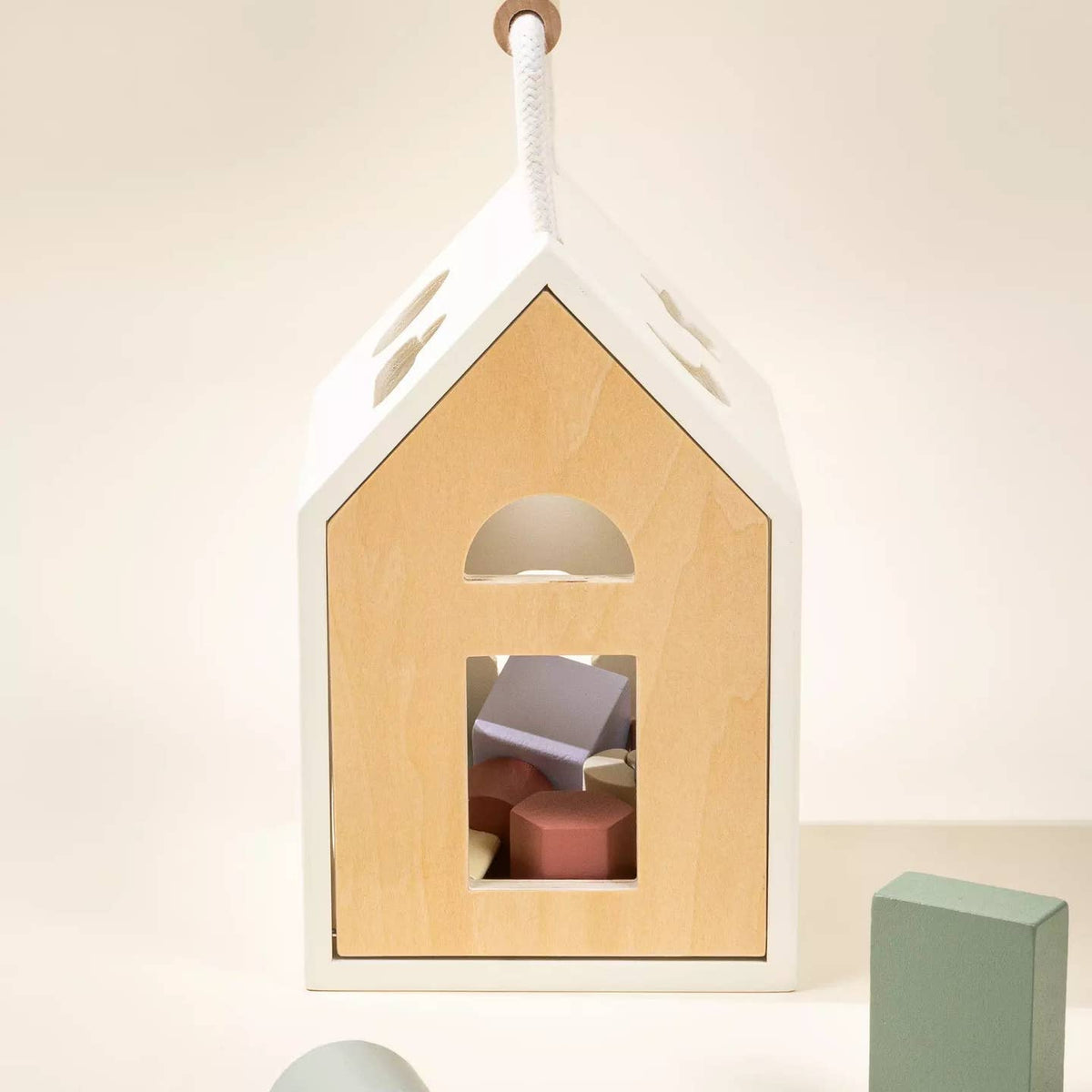 Wooden house-shaped toy with colorful blocks inside, hanging against a light background