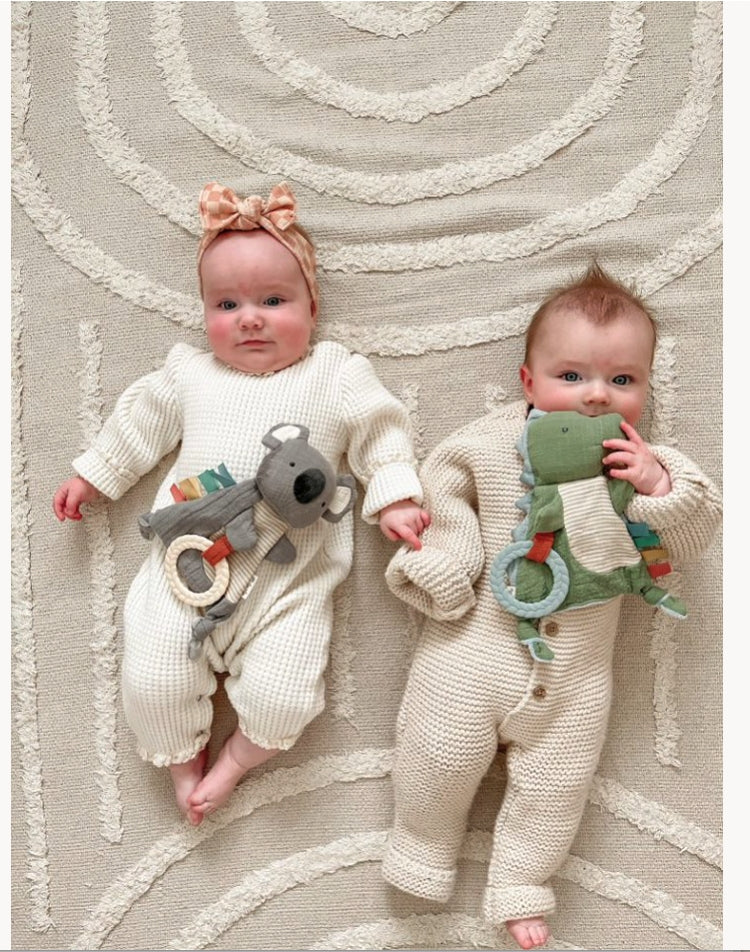 Two babies in knitted outfits with toys on a textured rug