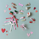 Collection of colorful hair clips and ribbons on a light blue background with heart shapes.