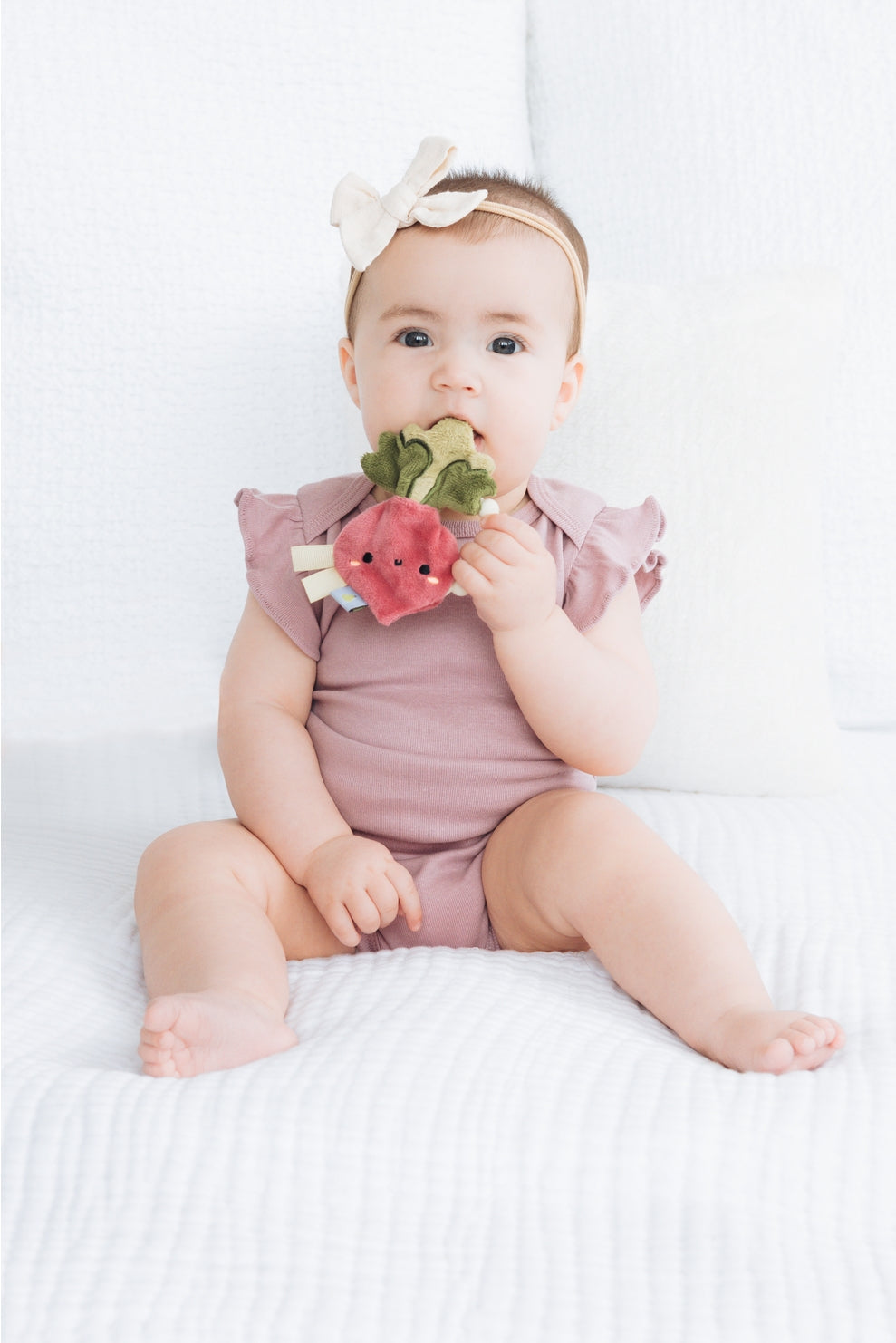 Baby in a pink outfit holding a watermelon-shaped toy on a white background