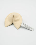 A cream-colored felt fortune cookie with a white paper tag attached that reads 'YOU WILL CATCH THE MOUSE' in black text, set against a plain light gray background.