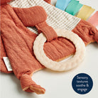 Textured orange baby blanket with a white ring and colorful clips on a neutral background.