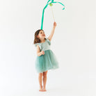 Young girl in a light blue dress holding a green ribbon against a white background