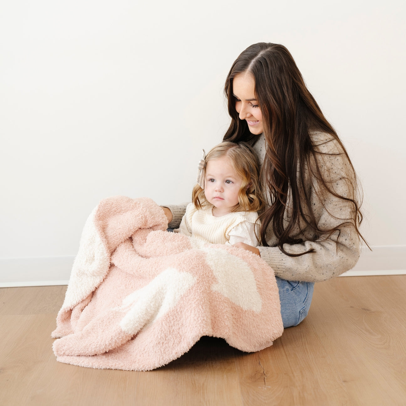 Woman and child sitting on a wooden floor with a pink blanket
