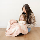 Woman and child sitting on a wooden floor with a pink blanket