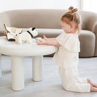 Child playing with a toy dog on a small table in a bright room.