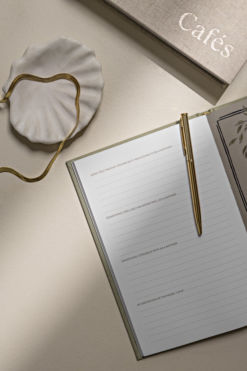 Notebook with a gold pen on a beige surface, with 'Cafés' text in the background.