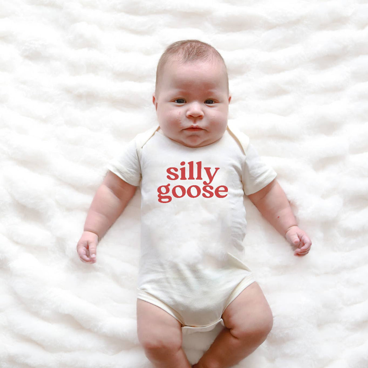 Baby wearing a white onesie with 'silly goose' text on a white blanket