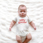 Baby wearing a white onesie with 'silly goose' text on a white blanket