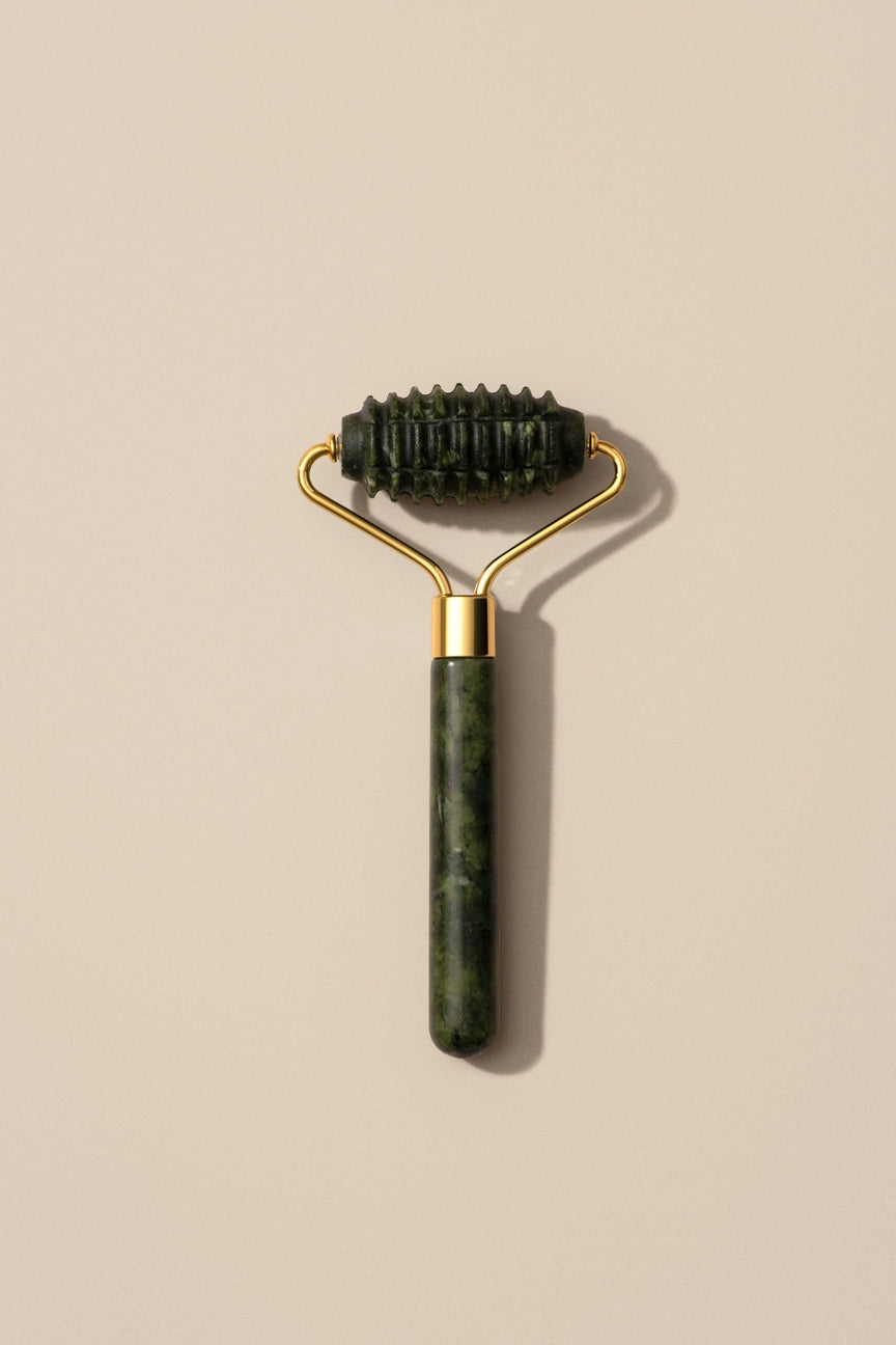 Green jade roller with gold handle on a beige background
