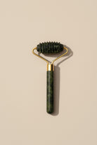 Green jade roller with gold handle on a beige background