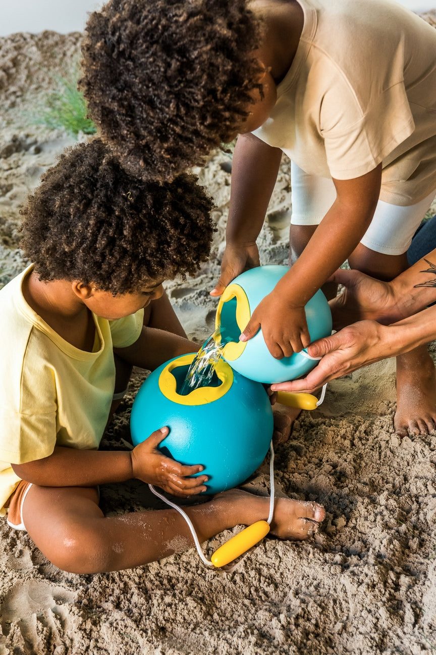Two children playing with colorful water toys on a sandy beach.