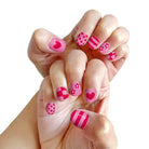 Close-up of hands with pink nail polish featuring various patterns on a white background