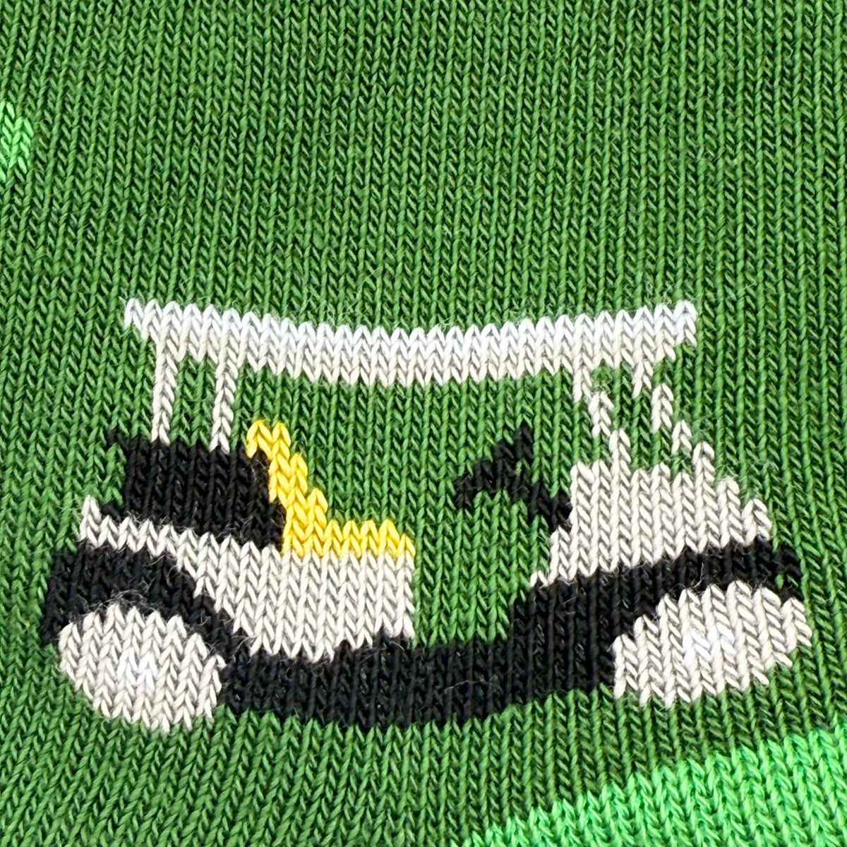 Close-up of a green knit garment featuring a knitted golf cart design in white, black, and yellow.