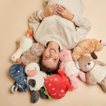 Person lying on a beige surface surrounded by various plush toys