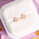 Smiley face earrings on a white cloth with a pink background