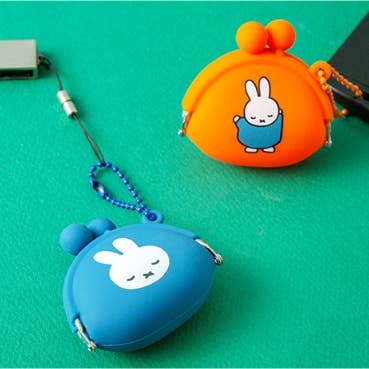 Two small pouches, one orange and one blue, with cartoon character designs on a green background.