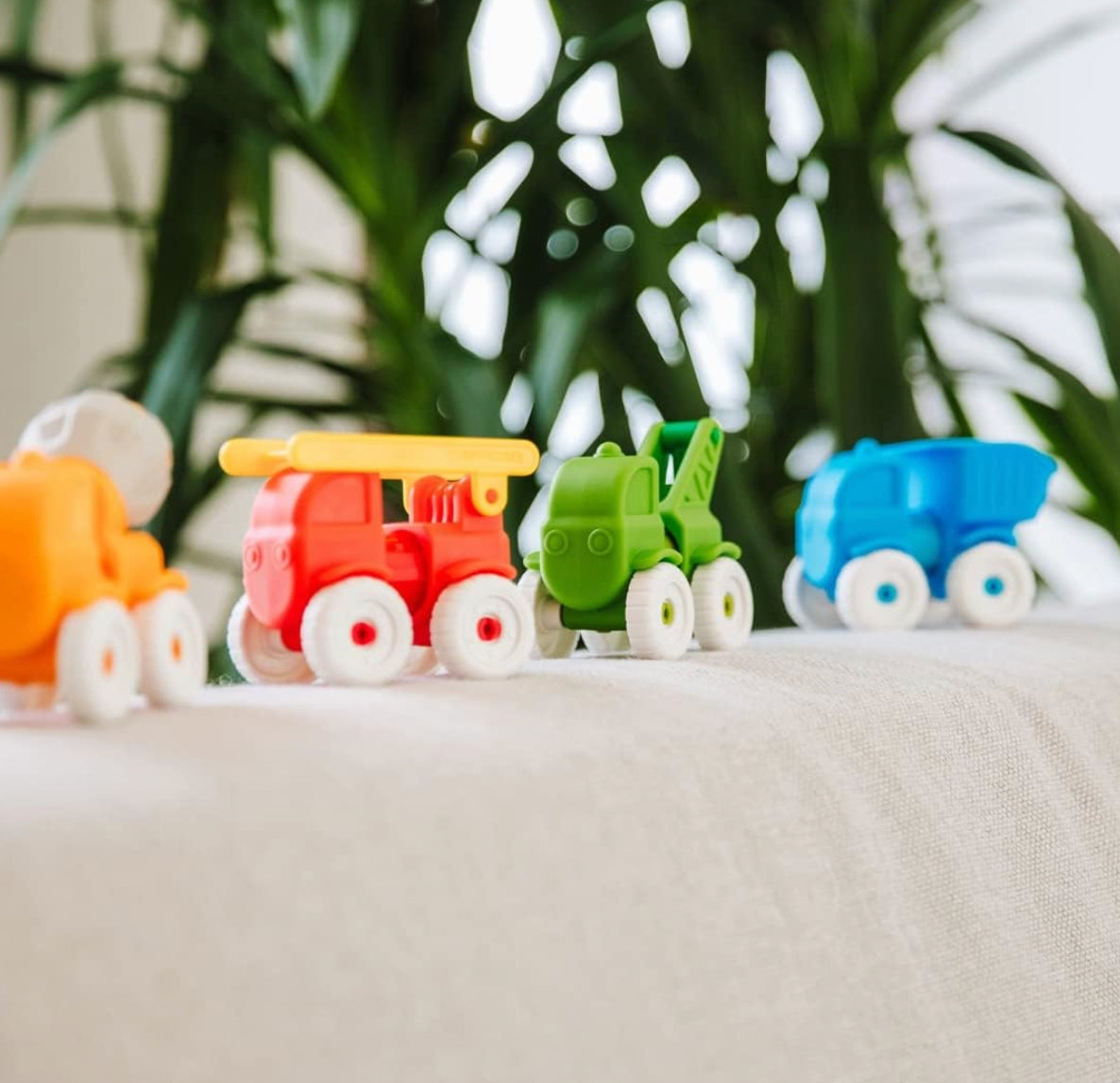 Colorful toy cars on a white surface with green plants in the background