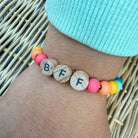 Colorful bracelet with letter beads on a wrist against a woven background