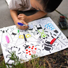 Child coloring a sheet of paper with insect illustrations outdoors.