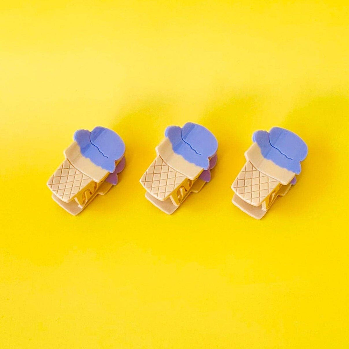 Three ice cream cone-shaped clips with blue lids on a yellow background