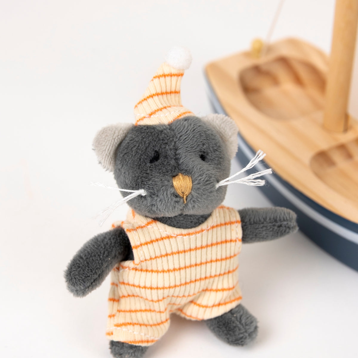 Small plush toy cat in an orange and white striped outfit on a light background