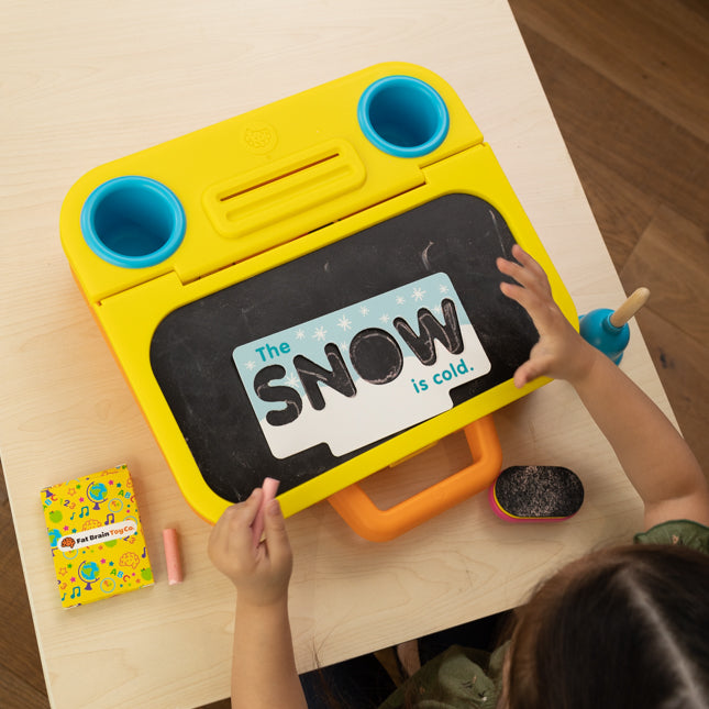 Child interacting with a yellow toy chalkboard on a wooden table