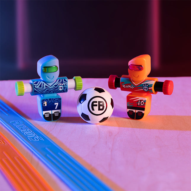 Two toy robots and a soccer ball on a reflective surface with a colorful background