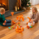 Two children playing with a colorful toy marble run set on a wooden floor.