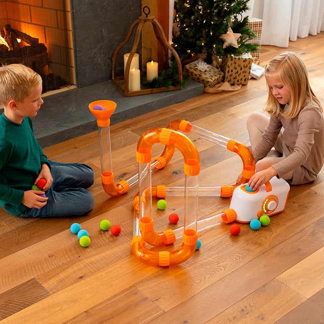 Two children playing with a colorful toy marble run set on a wooden floor.