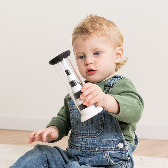 Child holding a transparent hourglass with black and white components on a light wooden floor.
