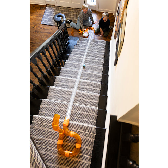Stair runner with orange clips on a staircase, children playing at the top.